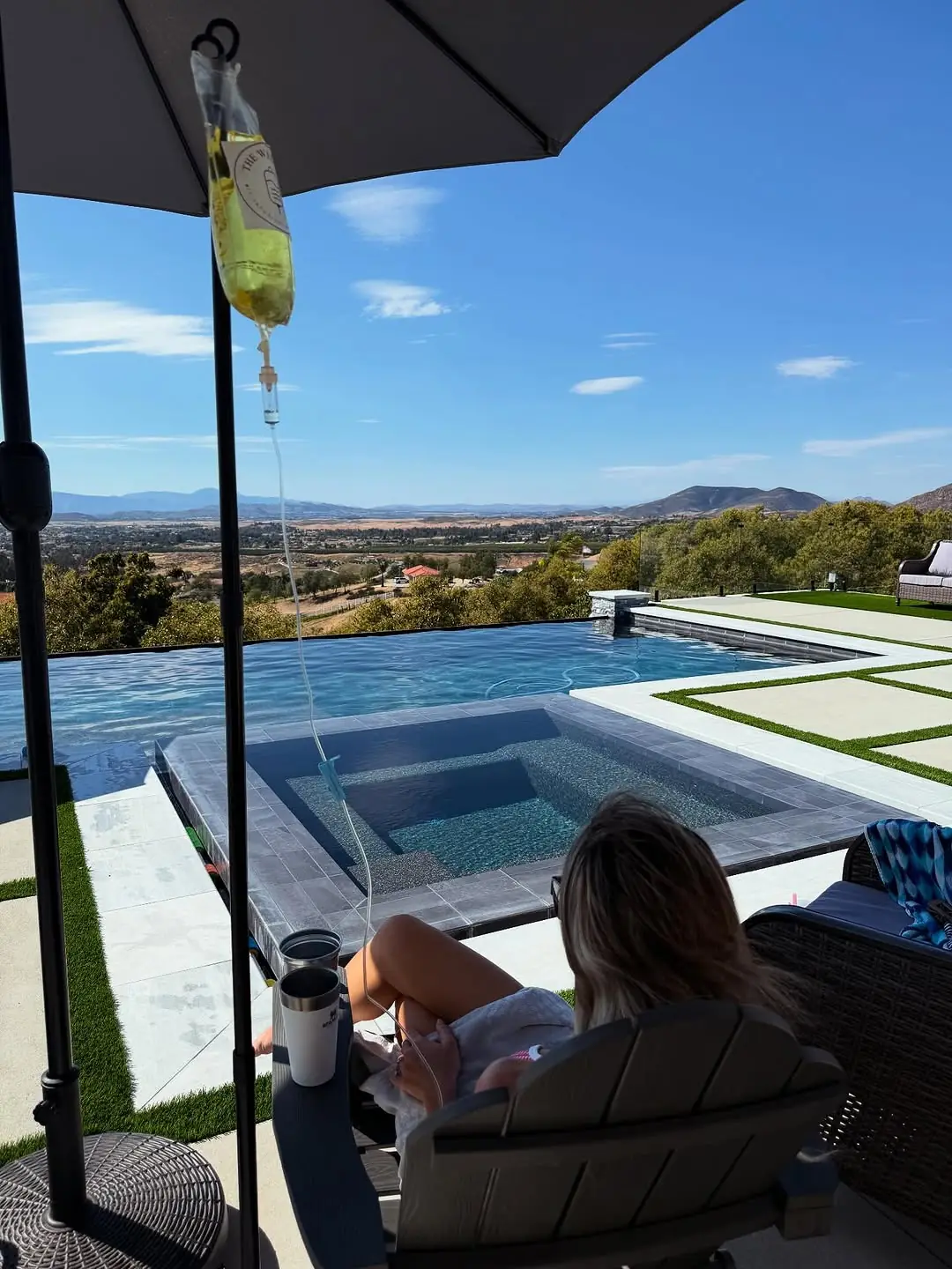 An IV drip bag from The Well Company hangs poolside overlooking the Temecula wine country hills