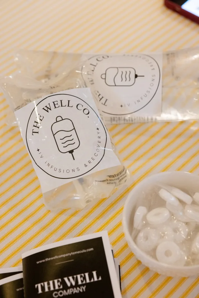 Two branded The Well Company IV bags and a printed brochure on the company's yellow-striped fabric